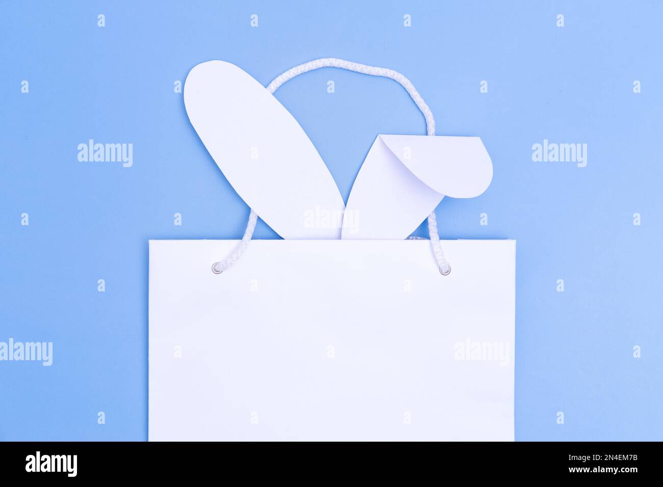 Ostern einkaufen. Weiße Einkaufstasche aus Papier mit weißen Hasenohren auf blauem Hintergrund. Konzept Ostergeschenke, Vorbereitung, Weihnachtsüberraschung. Stockfoto