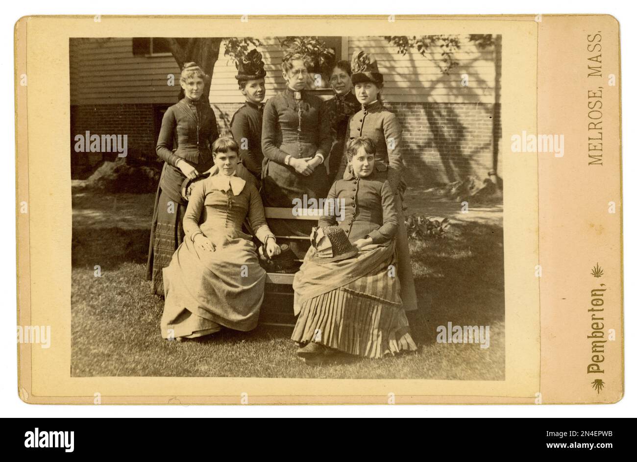 Originale Kabinettskarte aus der amerikanischen viktorianischen Ära einer entspannten Gruppe glücklicher Frauen, die vor einem Haus sitzen, das möglicherweise gerade erst gebaut wurde, da es Stapel von Baumaterial im Hintergrund gibt. Es gibt sie im hellen Sonnenschein. Sie tragen Kleider mit dem modischen Treiben auf der Rückseite und tragen oder halten die modischen Blumentöpfe in der Hand. Studio von Pemberton, Melrose, Middlesex County, Massachusetts, USA Ungefähr 1885. Stockfoto