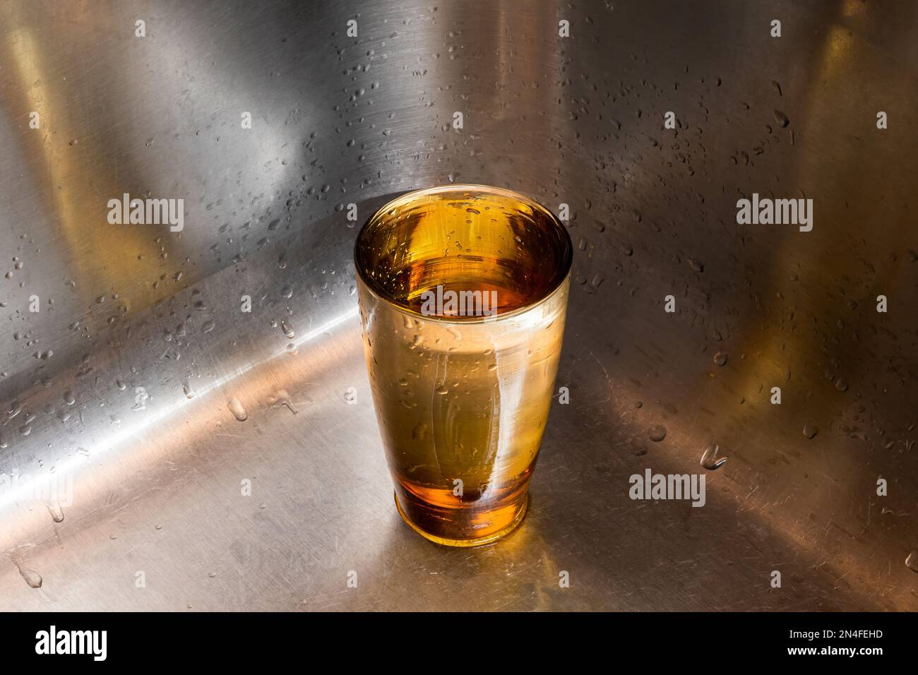 Ein volles Glas Wasser stand in der Ecke eines Spülbeckens aus Edelstahl mit viel Platz für umgekehrte Kopien. Stockfoto