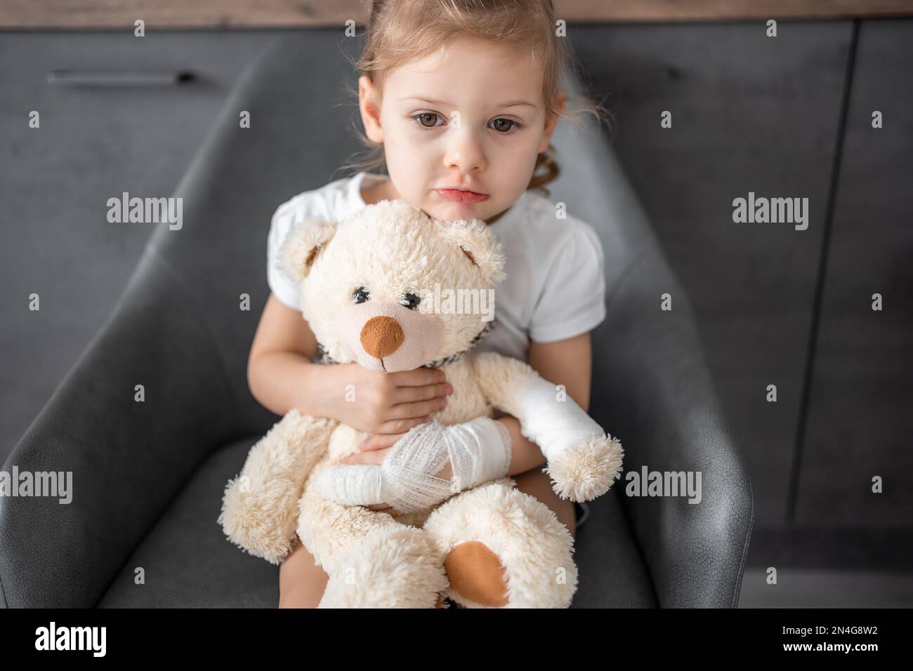 Ein kleines Mädchen mit gebrochenem Finger hält Teddybär mit einer ...