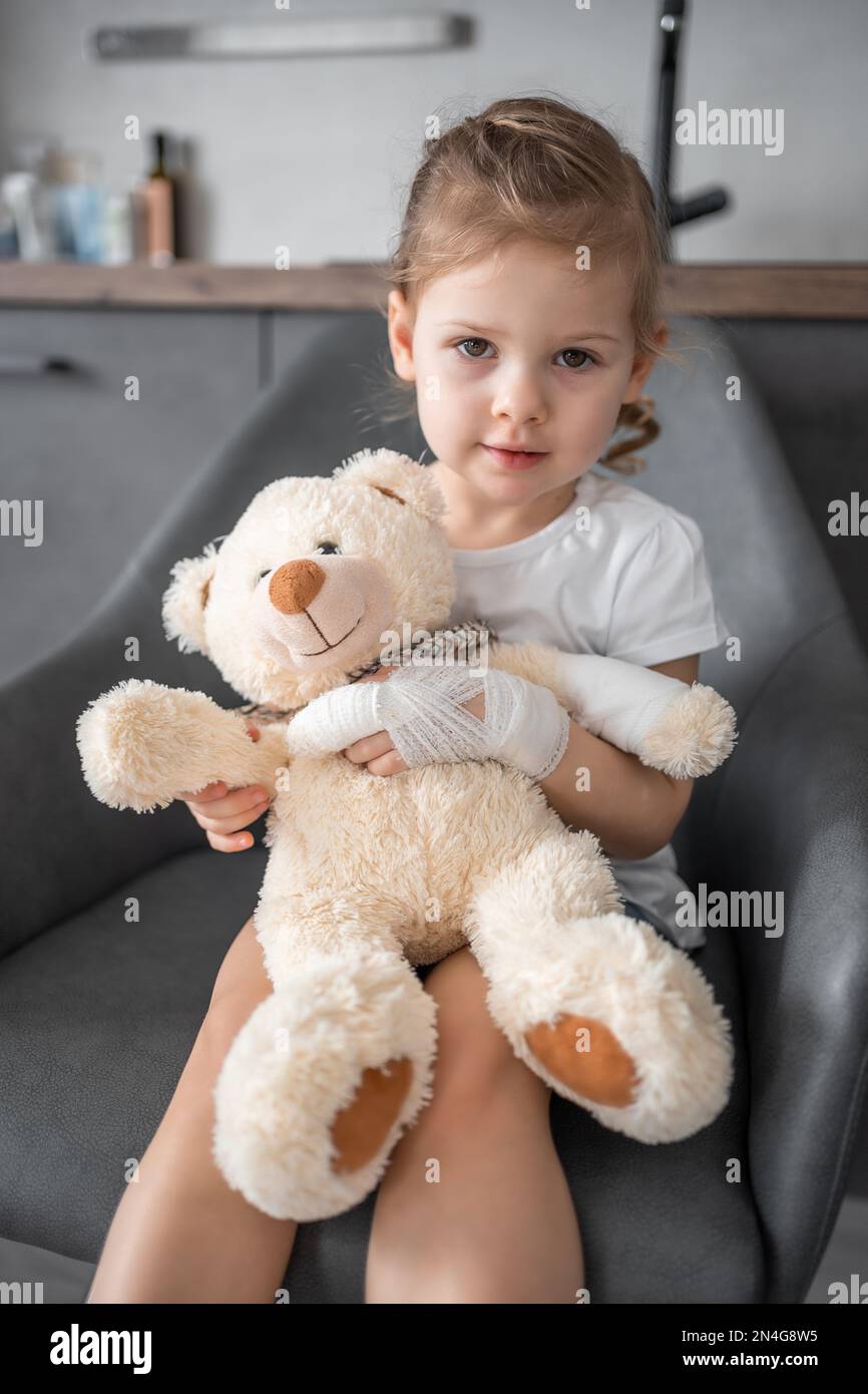 Ein kleines Mädchen mit gebrochenem Finger hält Teddybär mit einer ...