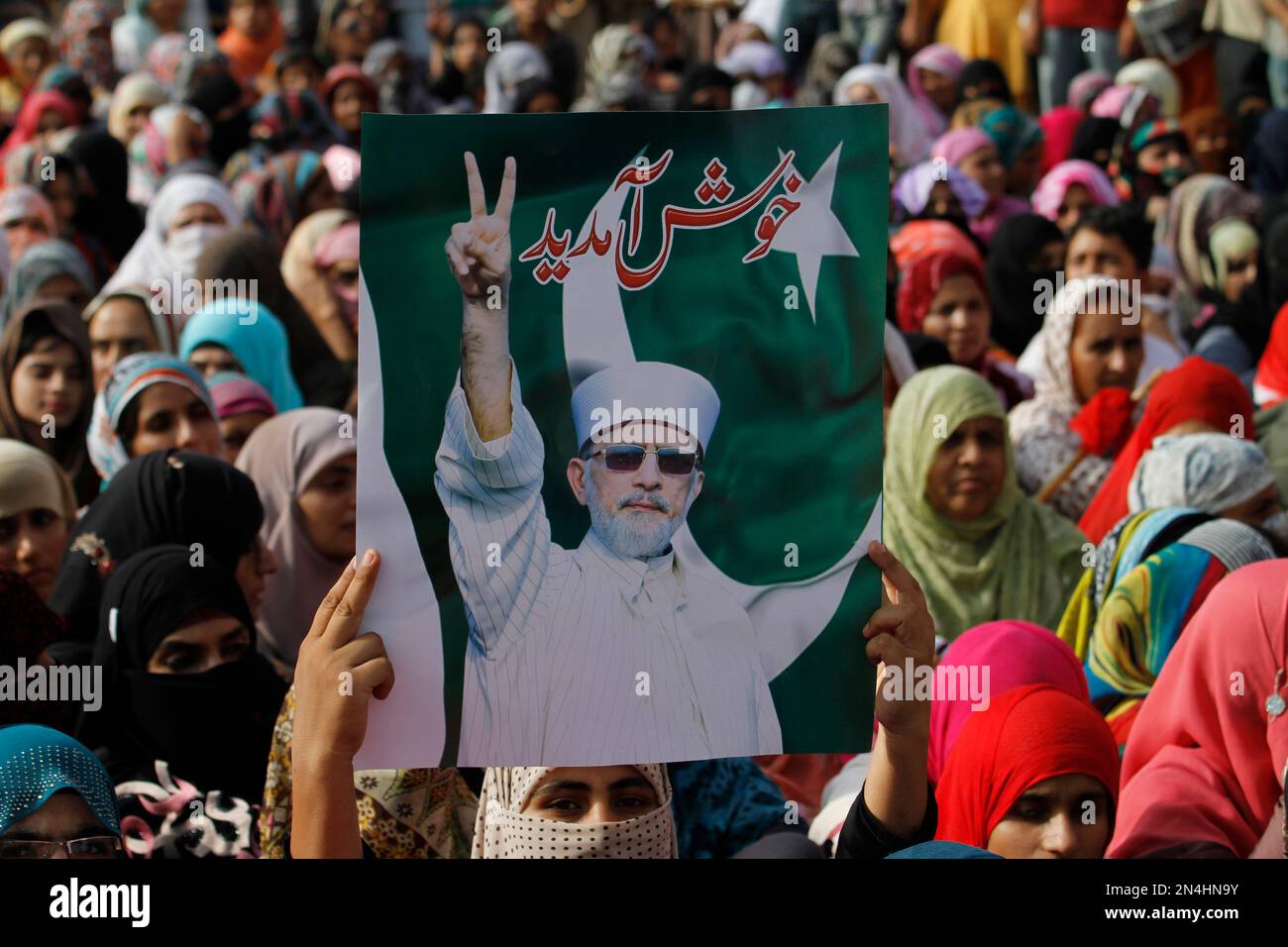 Supporters of Pakistani Muslim cleric Tahirul Qadri, leader of Pakistan Awami Tehreek (PAT) wait at Benazir International airport to receive their leader in Islamabad, Pakistan, Monday, June 23, 2014. The government has diverted the flight to Lahore due to security concern. Writing on a placard reads "welcome." (AP Photo/Anjum Naveed) Stockfoto