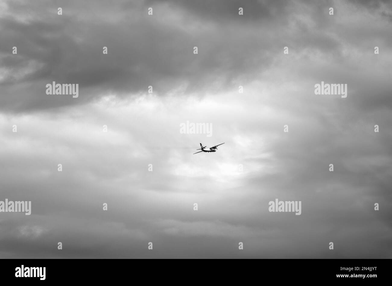 Schwarzweißfoto eines gefährlichen Flugzeugs, das in dunklen Wolken hoch oben am Himmel fliegt. Stockfoto