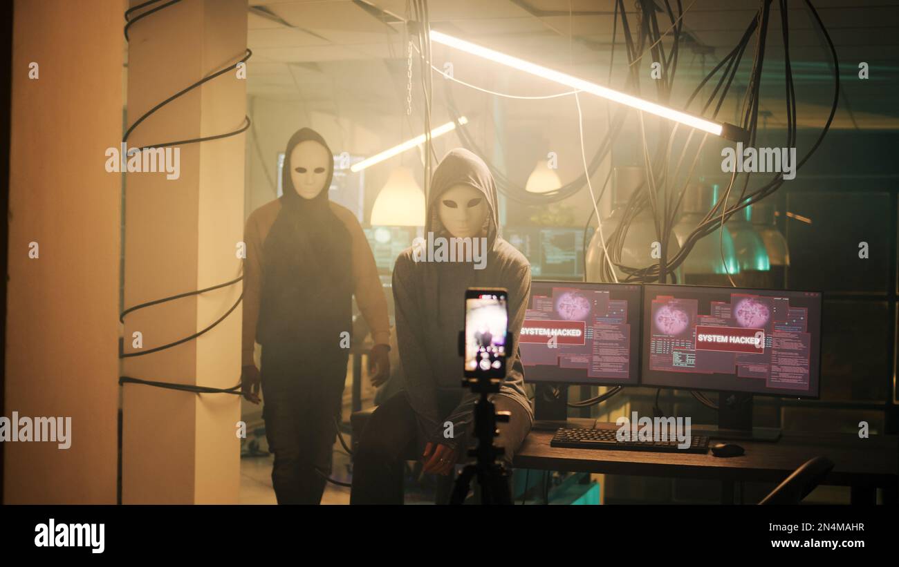 Team anonymer Personen, die ihre Identität verbergen, während sie ein Bedrohungsvideo für Ransomware aufzeichnen und wertvolle Regierungsinformationen im Dark Web verbreiten. Hacker mit Masken senden Live-Montage. Stockfoto