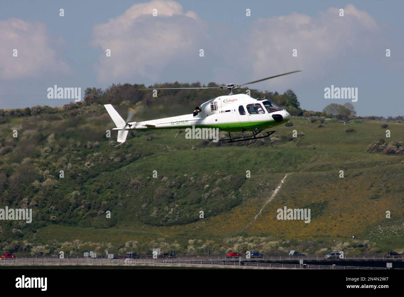 Ein Eurocopter AS 355N Ecureuil 2 Hubschrauber fliegt am Brighton City Airport mit South Downs hinten Stockfoto