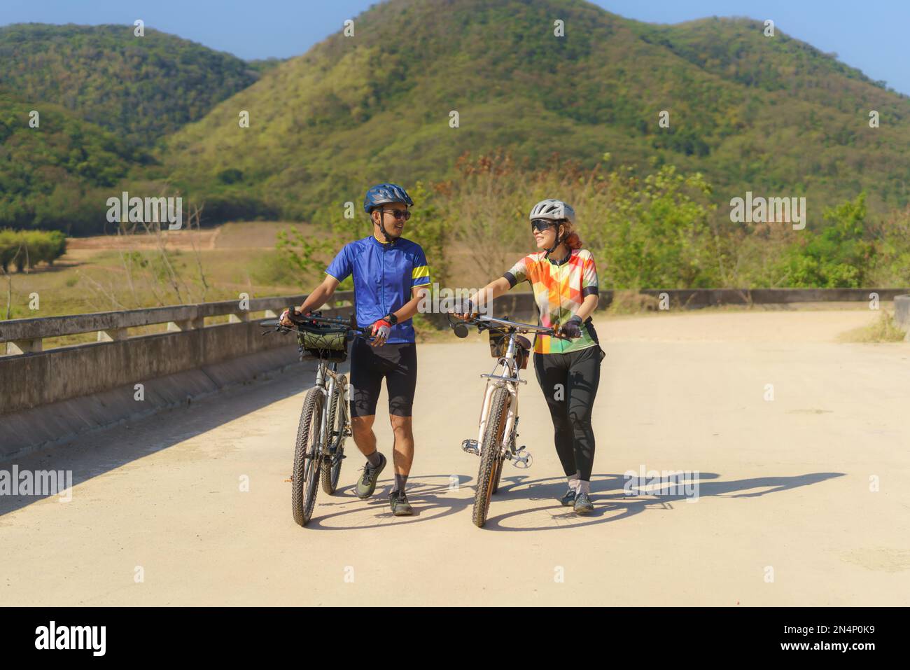 Asiatisches Fahrradpaar, das eine Pause vom Radfahren macht, macht eine Pause, geht spazieren und redet miteinander, um sich zu entspannen. Stockfoto
