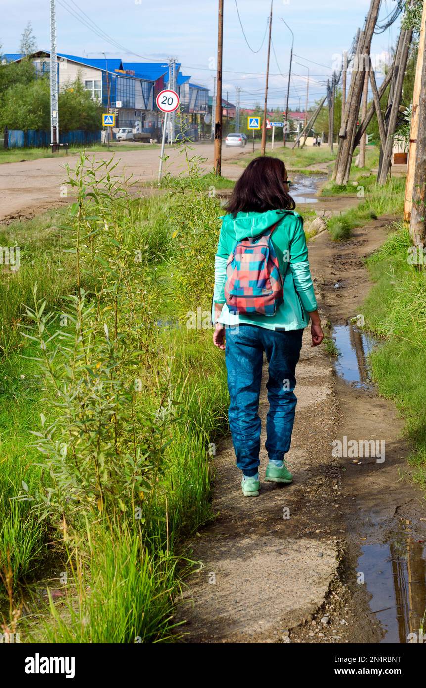 Das sportliche Yakut-Mädchen mit Rucksack-Lichtspaziergang geht entlang des alten Bürgersteigs nördlich des Dorfes Suntar. Stockfoto