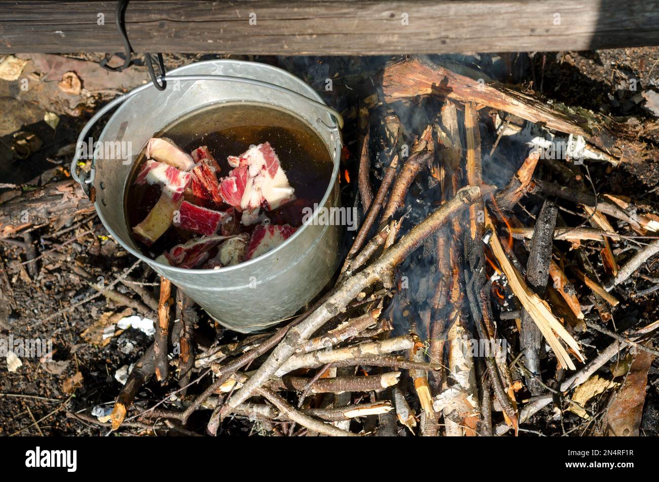 Fleischstücke schwimmen in einem Eimer auf einem Lagerfeuer in der wilden Natur des Nordens neben dem frischen Holz. Essen im Ruhezustand. Stockfoto