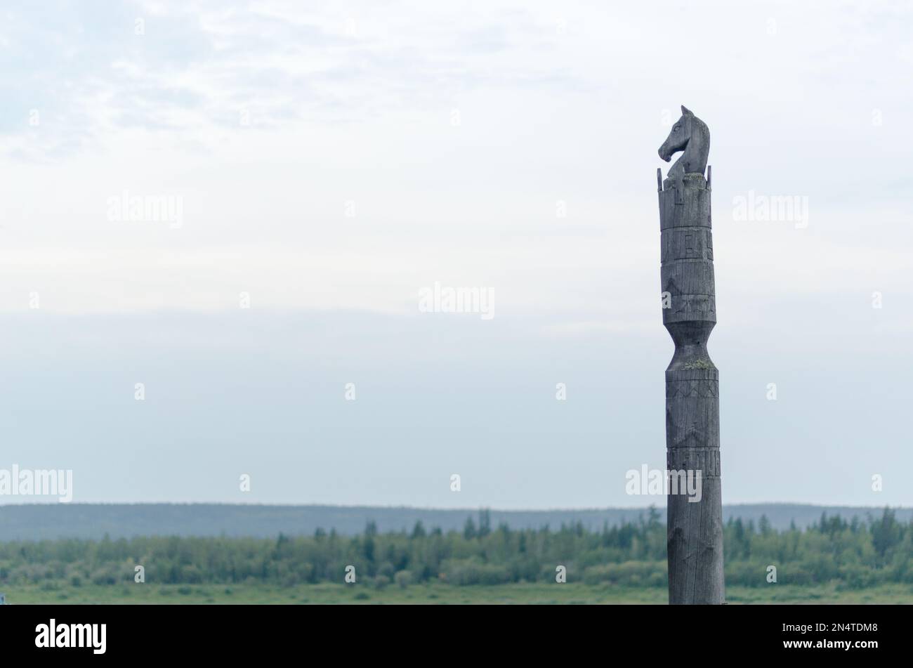 Yakut-Stange mit Pferd Serge steht mit dem Kopf eines Pferdes aus Holz auf einer Klippe vor endlosen Tundra und Wald unter den Wolken. Stockfoto
