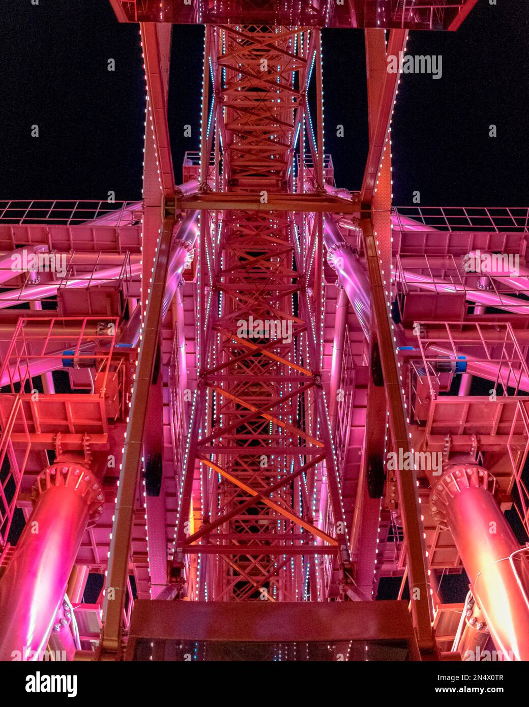 Ein leuchtend rotes Riesenrad mit einer großen Metallkonstruktion leuchtet und sorgt so für eine Feier im Dunkeln mit Licht. Stockfoto