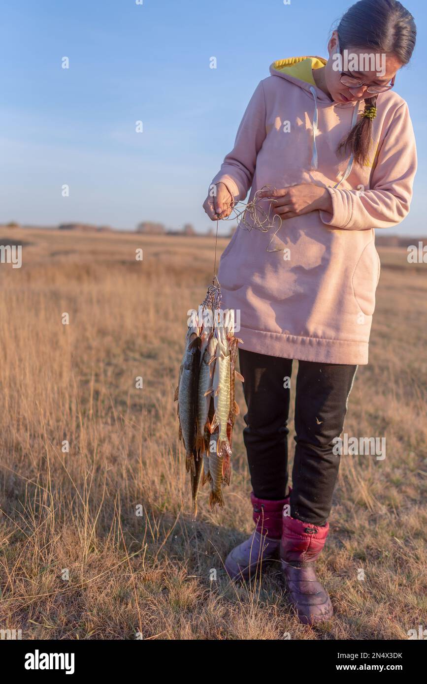 Yakut junge Fischerin mit einer Menge Fische hat Hechte gefangen, die auf dem Feld an Fish Stringer hängen. Stockfoto