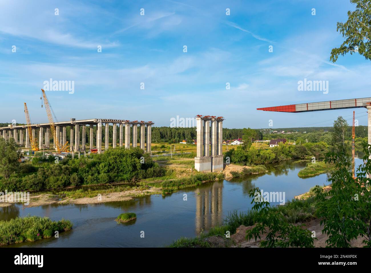 Bau einer Straßenbrücke über den Fluss. Verbindung von Spannen auf der Flusslinie beim Bau der nördlichen Umgehungsstraße im Sommer. Stockfoto