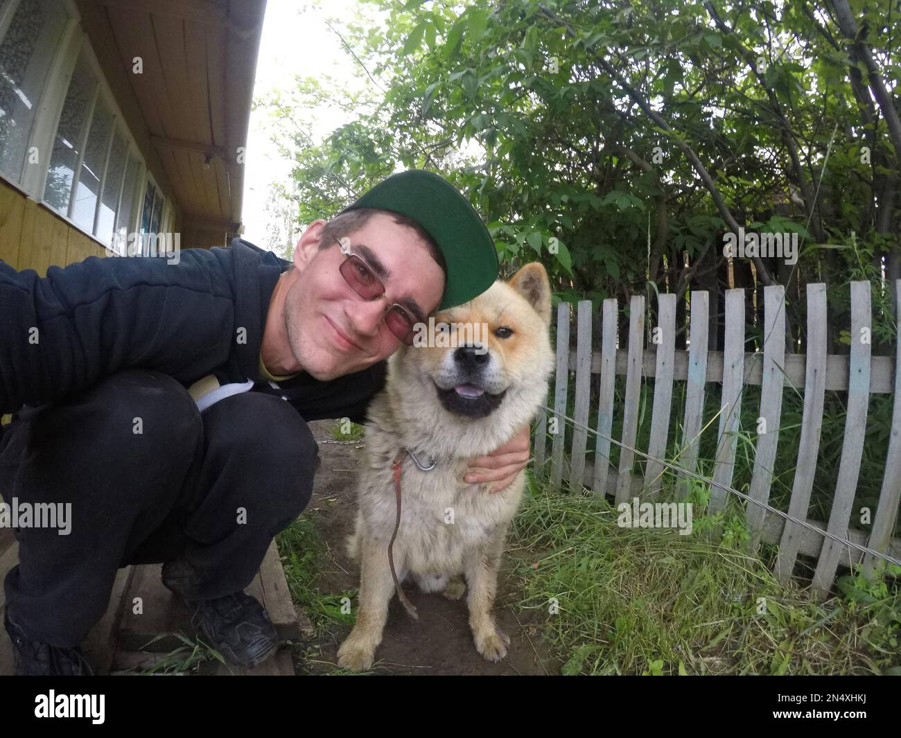 Ein russischer Mann mit Brille macht ein Selfie mit einer Hunderasse Akita inu auf dem Privatgelände eines Wohngebäudes in Yakutia. Stockfoto