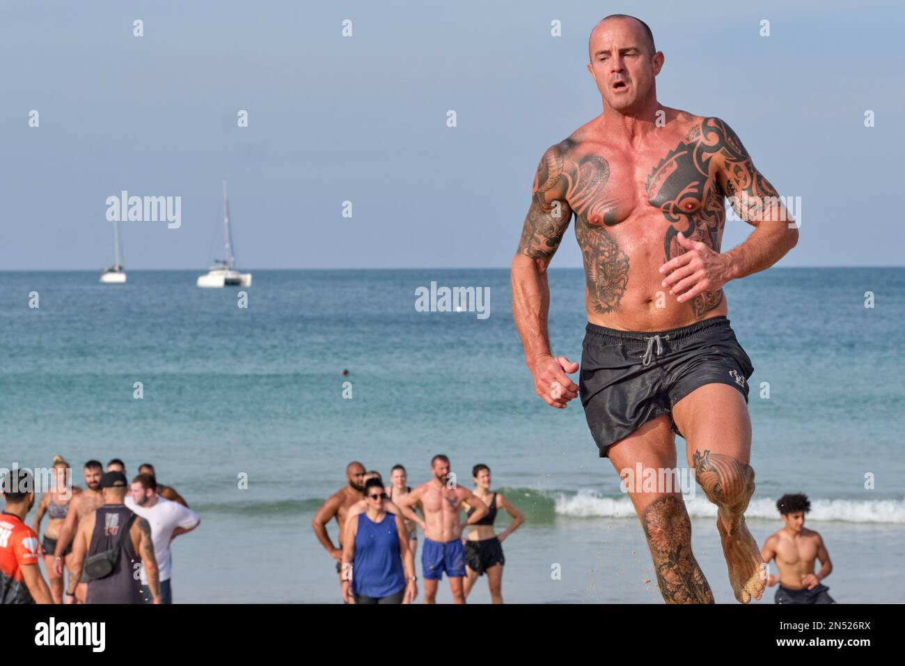 Ein tätowierter männlicher Tourist aus dem Westen, der im Rahmen einer von Touristen organisierten kleinen privaten Sportveranstaltung am Nai Harn Beach, Phuket, Thailand, unterwegs ist Stockfoto