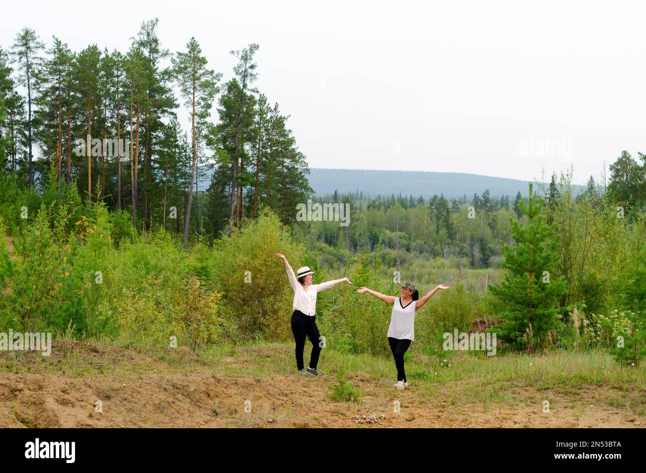 Yakut asiatische Mädchen posieren mit erhobenen Händen und stehen am Hang von Homa vor dem Hintergrund des nördlichen Taiga-Waldes. Stockfoto