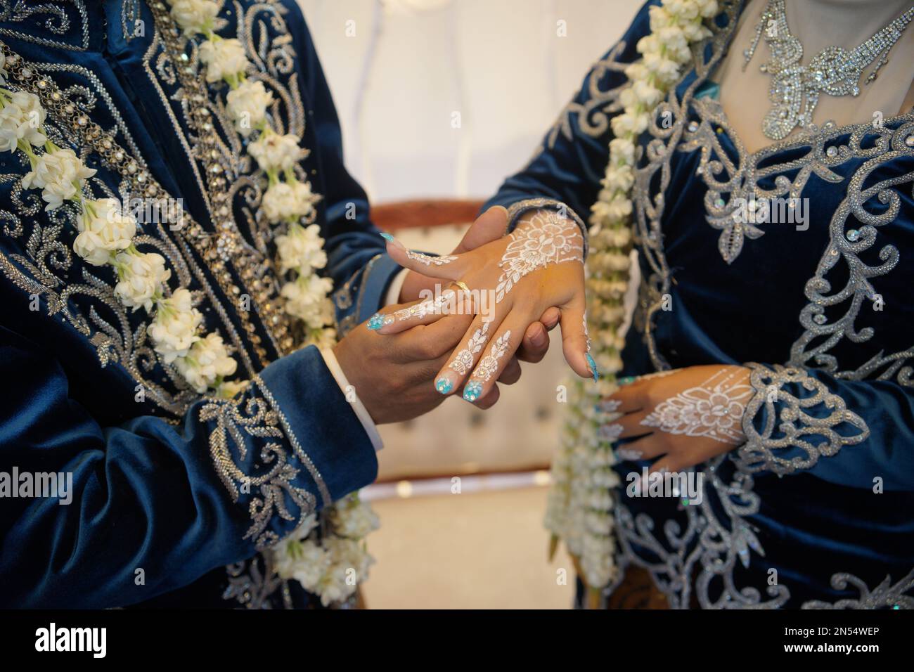 Der Bräutigam legt den Hochzeitsring auf die Hand der Braut und trägt in einer traditionellen Hochzeitszeremonie ein Hochzeitskleid mit Jasmine- und Magnolienblumen Stockfoto