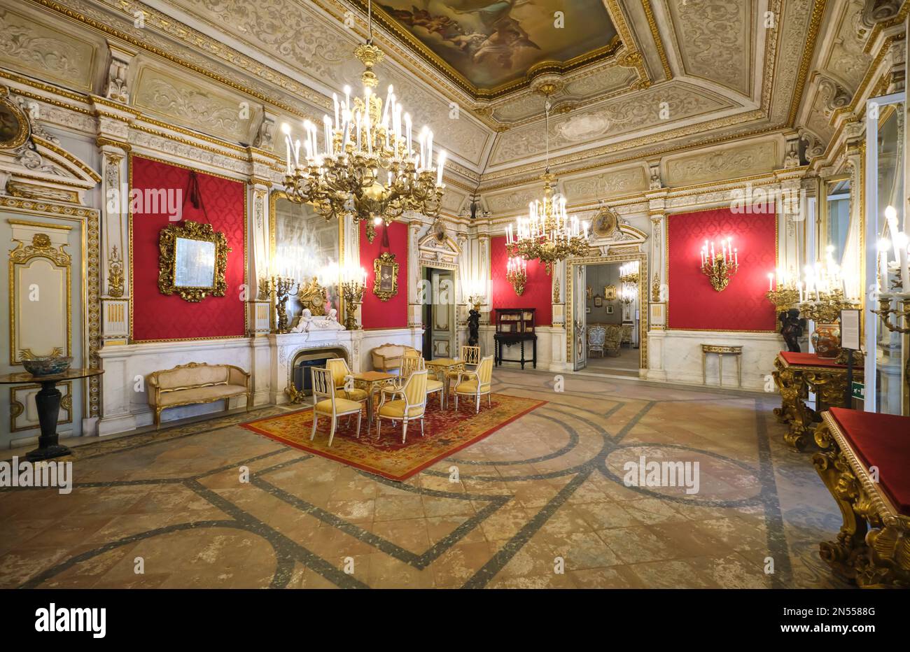 Ein großer antiker Wohnraum mit roter Tapete, Spiegeln, Deckengemälde und Kronleuchtern. Im Herrenmuseum, Museo Pignatelli in Neapel, Neapel, Italien, Stockfoto