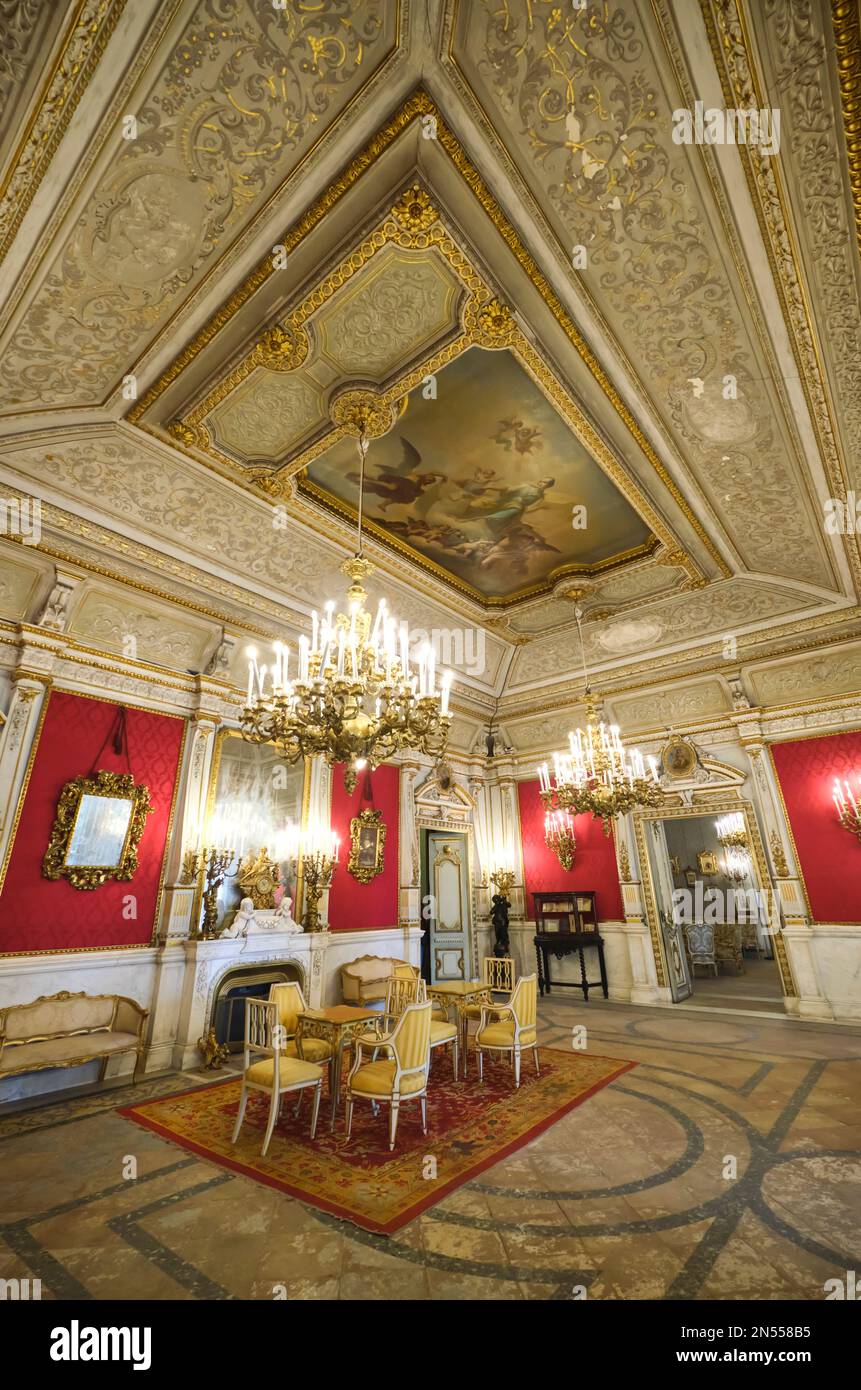 Ein großer antiker Wohnraum mit roter Tapete, Spiegeln, Deckengemälde und Kronleuchtern. Im Herrenmuseum, Museo Pignatelli in Neapel, Neapel, Italien, Stockfoto