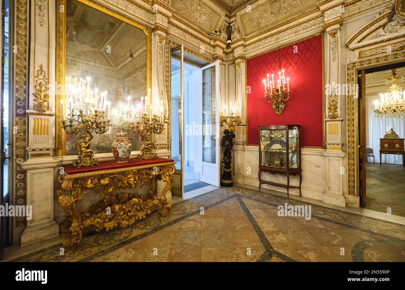 Eine Ecke eines historischen Zimmers mit goldenem Beistelltisch, Schrank, roter Tapete und großem Spiegel. Im Herrenmuseum, Museo Pignatelli in Neapel, Neapel, Italien Stockfoto