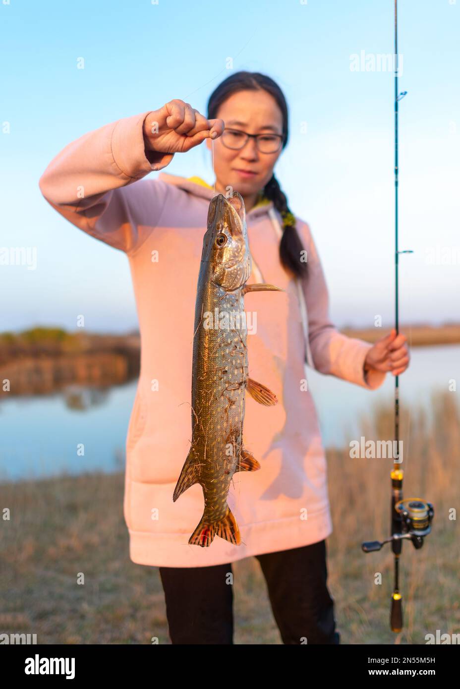 Yakut Mädchen Fischer hart in der Hand auf der Schnur hielt Hecht mit Spinnen in der anderen Hand auf dem Hintergrund des Sees gefangen. Stockfoto