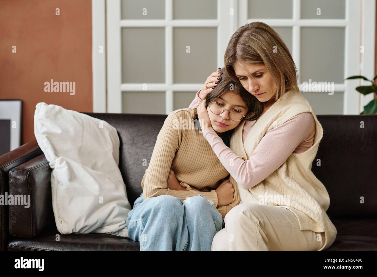 Die Mutter saß zusammen mit ihrer Tochter auf dem Sofa und umarmte sie, sie tröstete sie während einer Depression Stockfoto