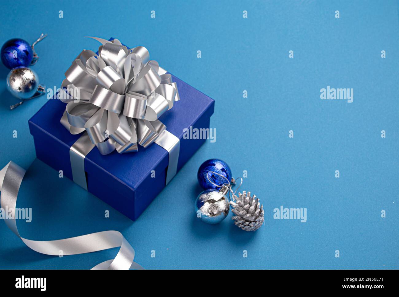 Weihnachtsgeschenkbox in blaues Papier mit silbernem Band und Schleife verpackt, Weihnachtskugeln Dekoration auf blauem Papierhintergrund mit Kopierbereich Stockfoto