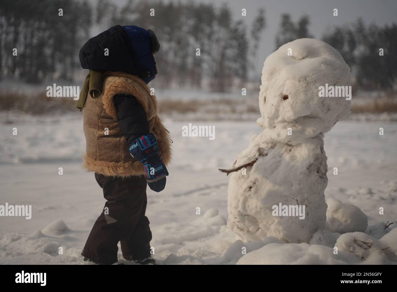 Der süße kleine Junge mit Ohrenschützenmütze macht einen Schneemann Stockfoto