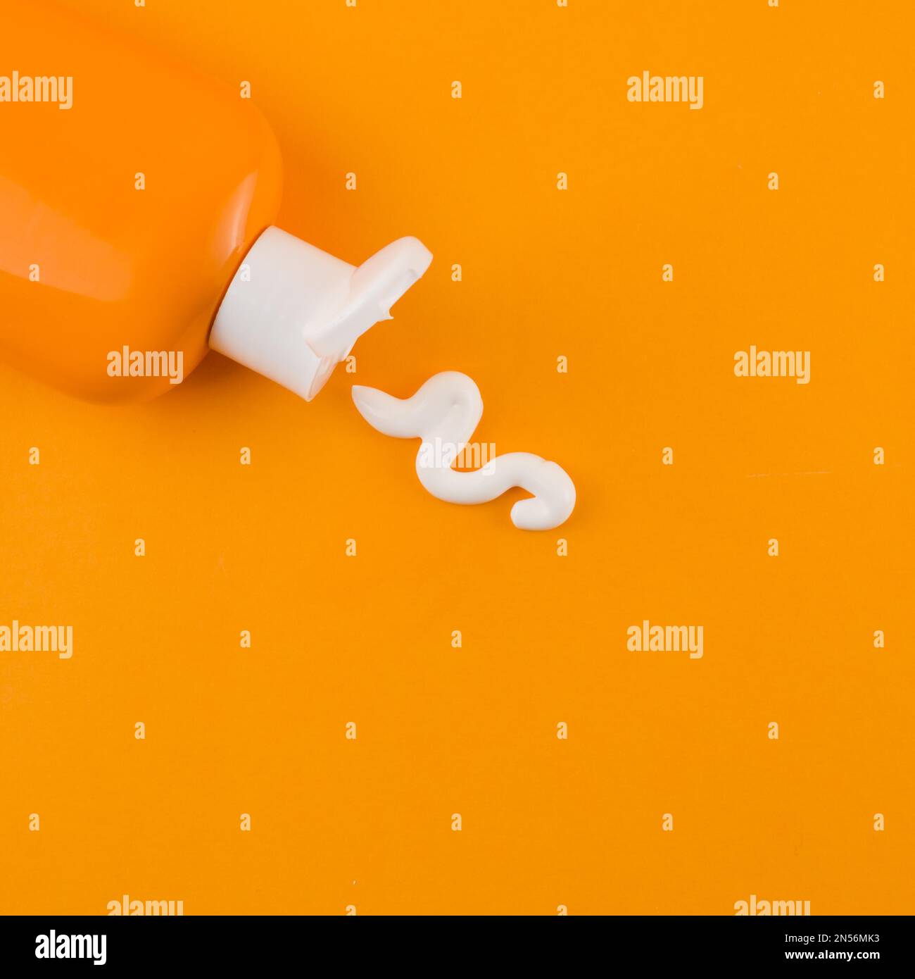 Weiße Sonnencreme, die aus der orangefarbenen Flasche vor orangefarbenem Hintergrund herauskommt. Auflösung und hochwertige Fotos Stockfoto