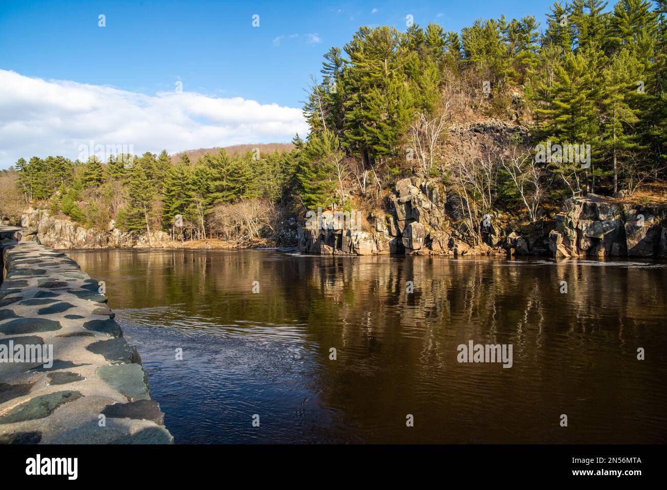 Wunderschöne Dalles of the St. Croix River mit zerklüfteten Klippen mit Kiefern entlang der Küste und einer Steinmauer am Fluss. Stockfoto