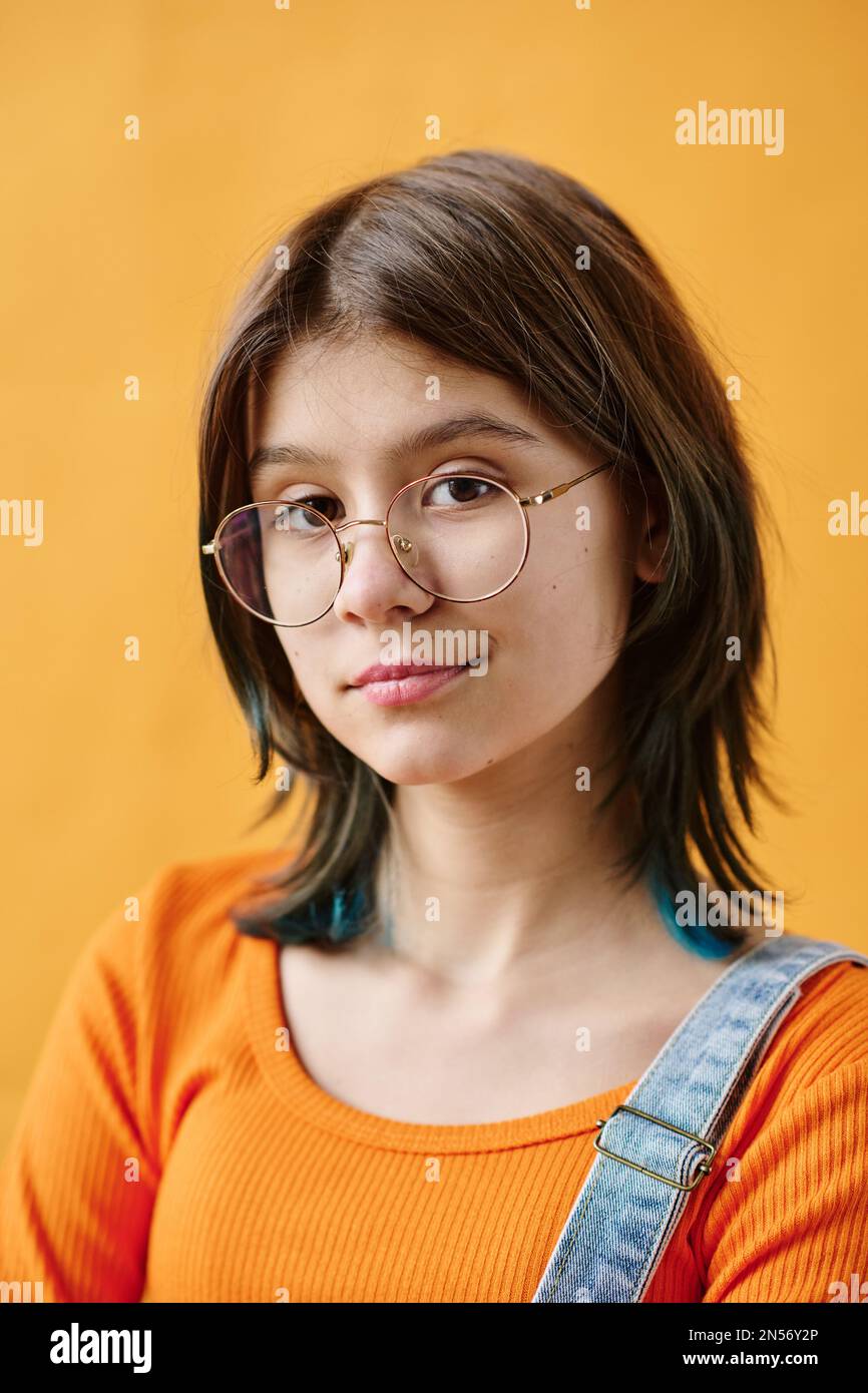 Porträt eines süßen Teenagers mit Brille, das isoliert auf orangefarbenem Hintergrund in die Kamera schaut Stockfoto