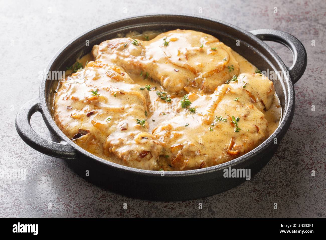 Gebratene würzige Schweinekoteletts und dann geschmorte in cremiger Zwiebelsoße auf dem Topf auf dem Tisch. Horizontal Stockfoto