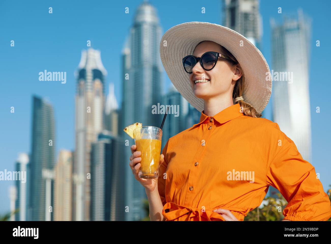 Glückliche Frau in Kleid und Sonnenhut mit Smoothie-Cocktail im Urlaub im Dubai Beach Resort Stockfoto