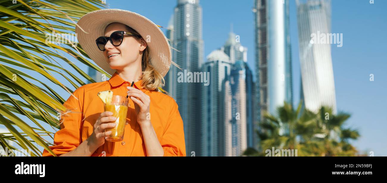 Lächelnde attraktive Frau in Kleid und Sonnenhut mit Smoothie-Cocktail im Urlaub im Dubai Beach Resort. Banner mit Kopierbereich Stockfoto