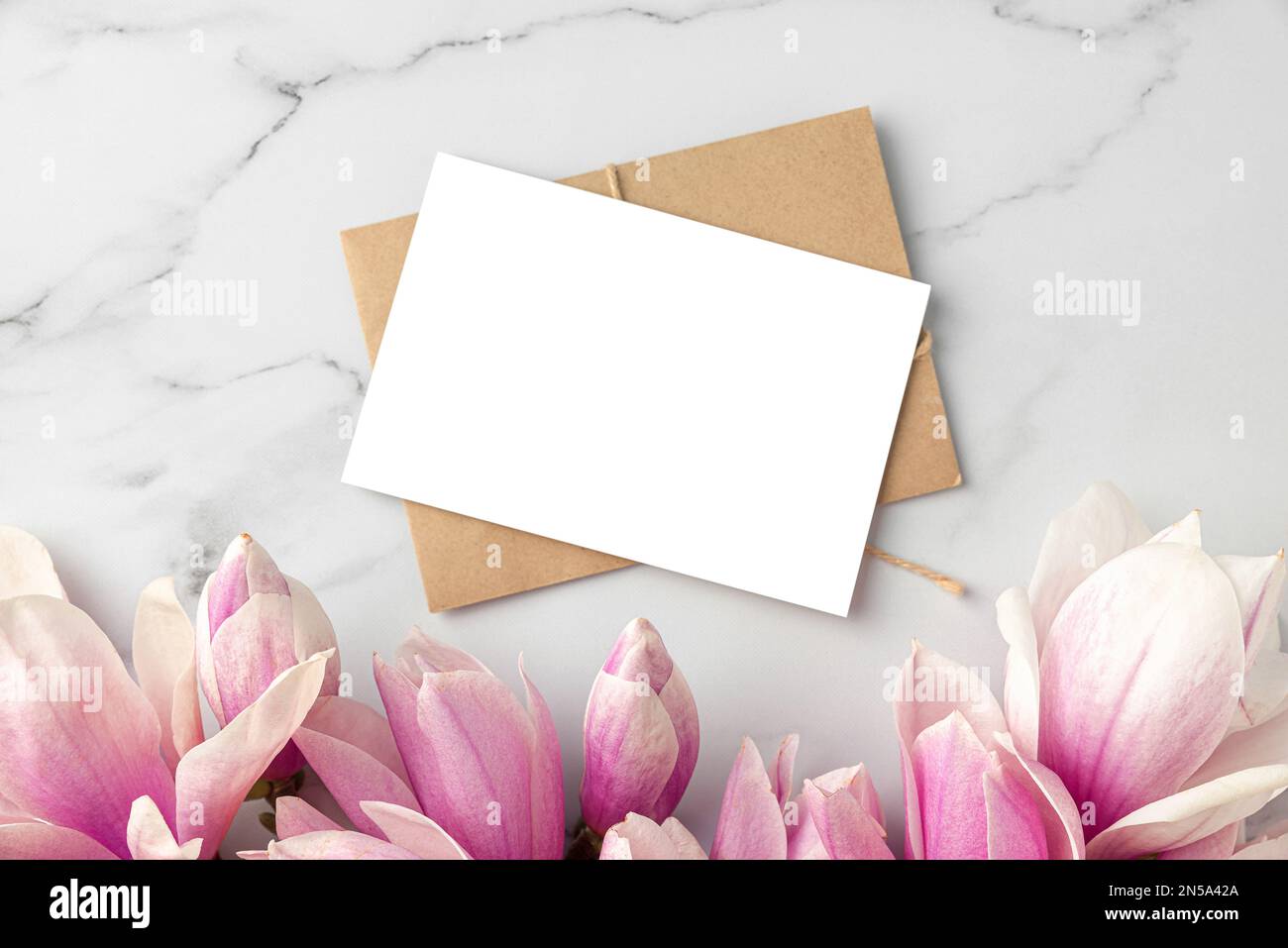 Leere Grußkarte oder Hochzeitseinladung mit pinkfarbenen Magnolienblumen auf weißem Marmorhintergrund. Modell. Flach verlegt Stockfoto