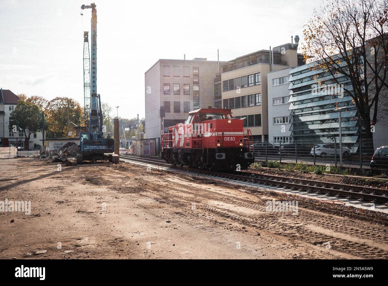 Eine alte Lokomotive in Rot fährt über die Schienen an einer Baustelle vorbei. Der Zug ist auf den Gleisen und die Sonne scheint in Köln. Stockfoto