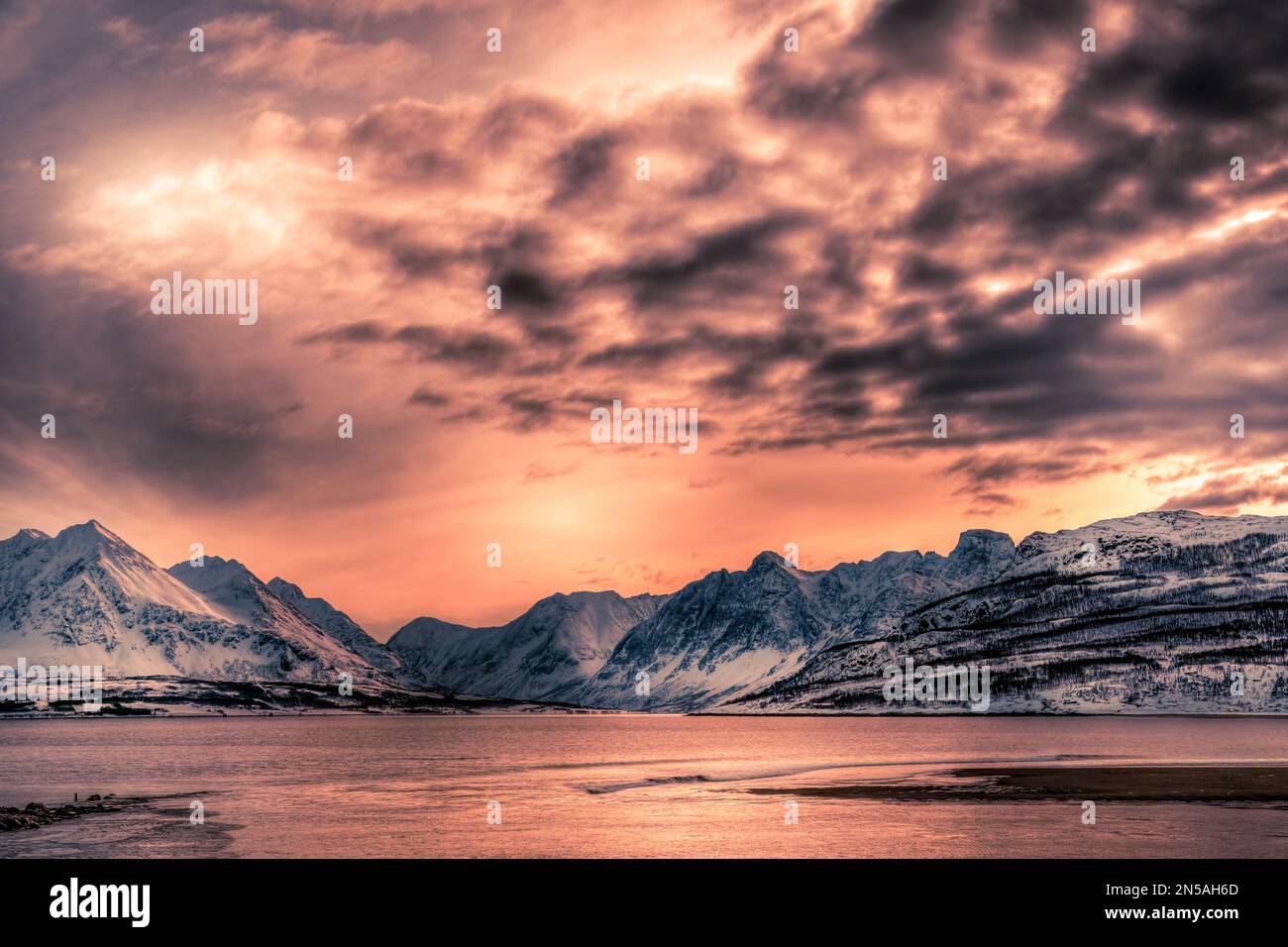 Ein atemberaubender Sonnenuntergang über einem See mit Blick auf die schneebedeckten Berge in der Nähe von Tromso im äußersten Norden Norwegens Stockfoto