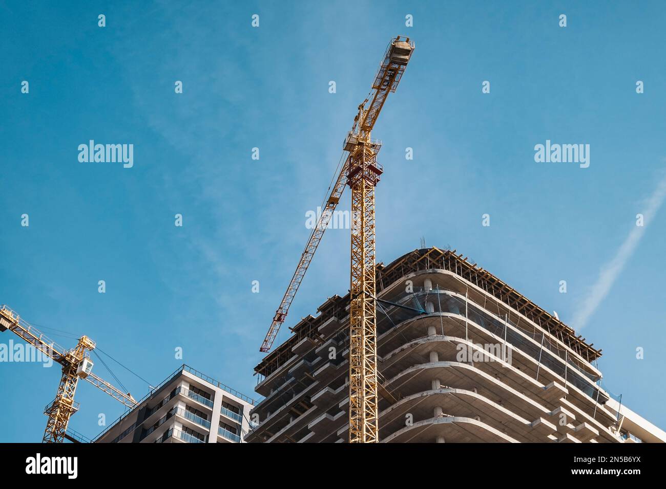 Kran und Baustelle vor blauem Himmel. Industrie für die Unterbringung von Neubauten. Industriekonzept Stockfoto