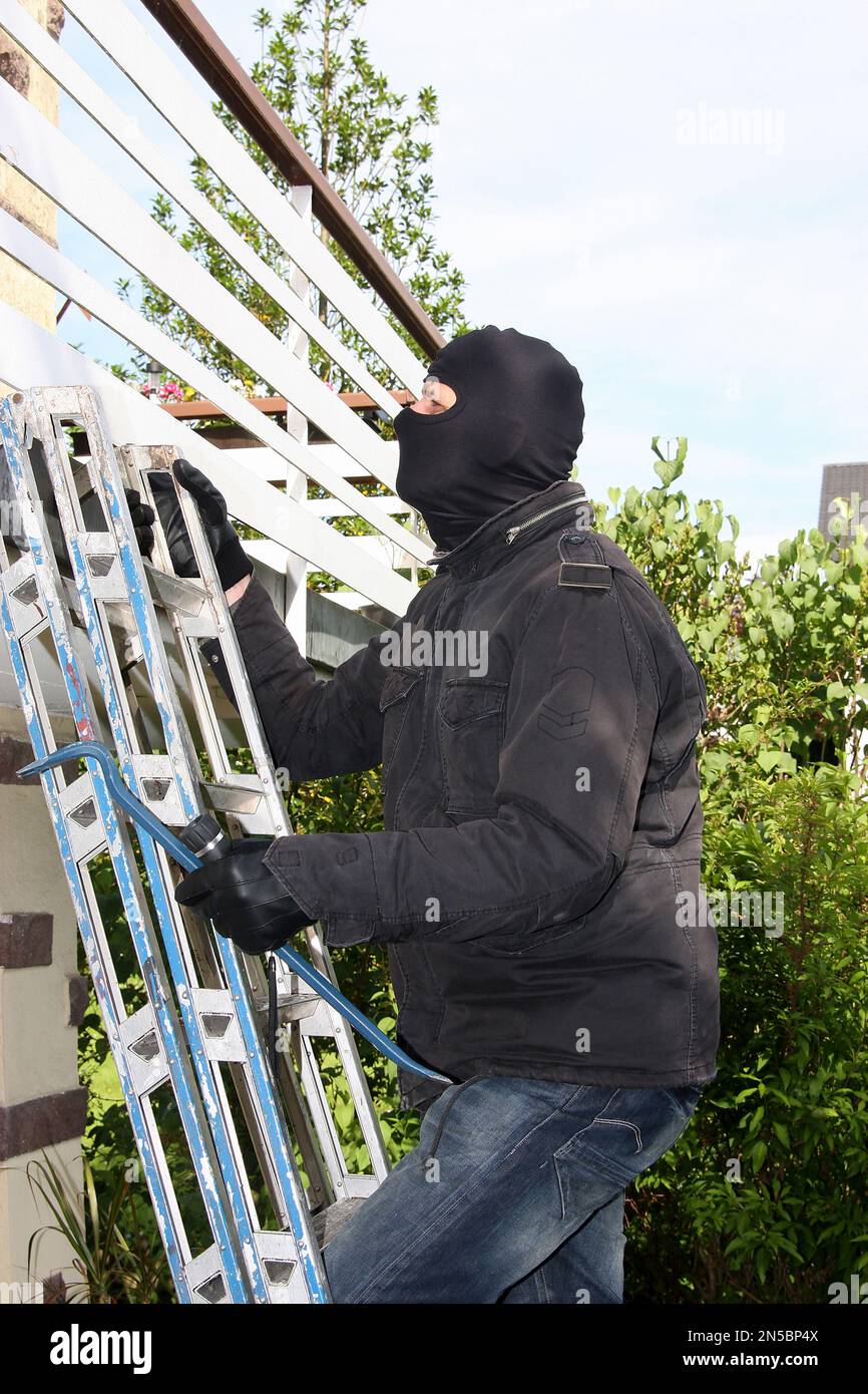 Einbrecher mit Brechstange und Taschenlampe auf einer Leiter auf einem Balkon Stockfoto