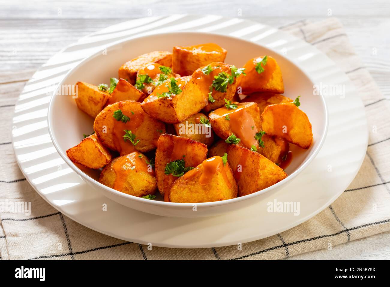 Patatas bravas, spanische frittierte Kartoffeln mit scharfer Sauce in weißer Schüssel auf weißem Holztisch, horizontale Sicht von oben Stockfoto
