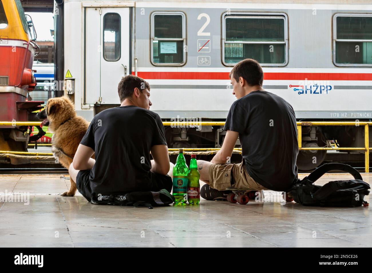 Zwei junge Männer, die sich unterhalten, mit ihrem Hund reisen, sitzen auf dem Bahnsteig Glavni Kolodvor. Zagreb, Kroatien, Europa, Europäische Union Stockfoto