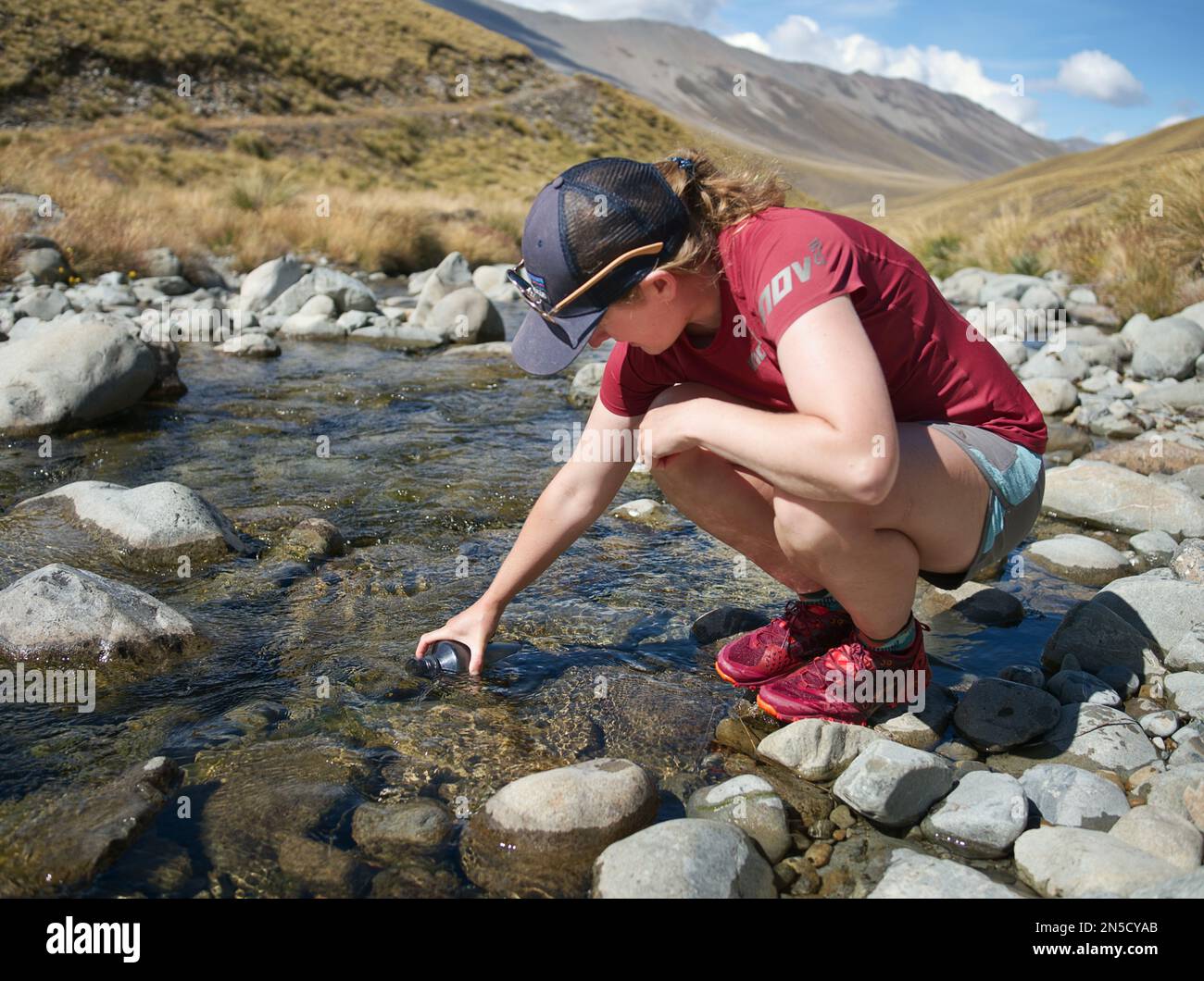 Eine Wanderer füllt ihre Wasserflasche aus einem klaren Süßwasserstrom auf Stockfoto
