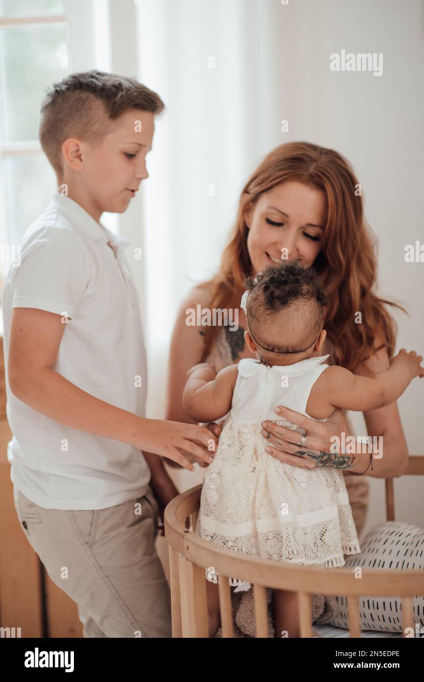 Gemischte Familie mit weißem Sohn und Tochter, die sich in einer gemütlichen Wohnung befindet. afroamerikanisches Baby mit seiner hellhäutigen mutter OL Stockfoto