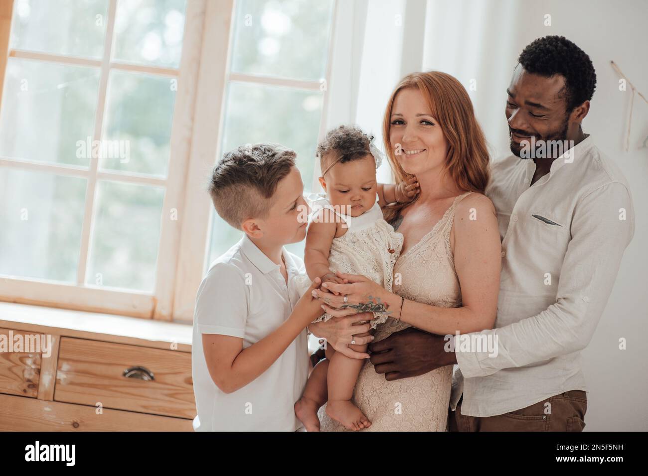 Gemischte Familie mit weißem Sohn und Tochter, die sich in einer gemütlichen Wohnung befindet. Ein afroamerikanischer Mann mit seiner hellhäutigen Frau Ki Stockfoto