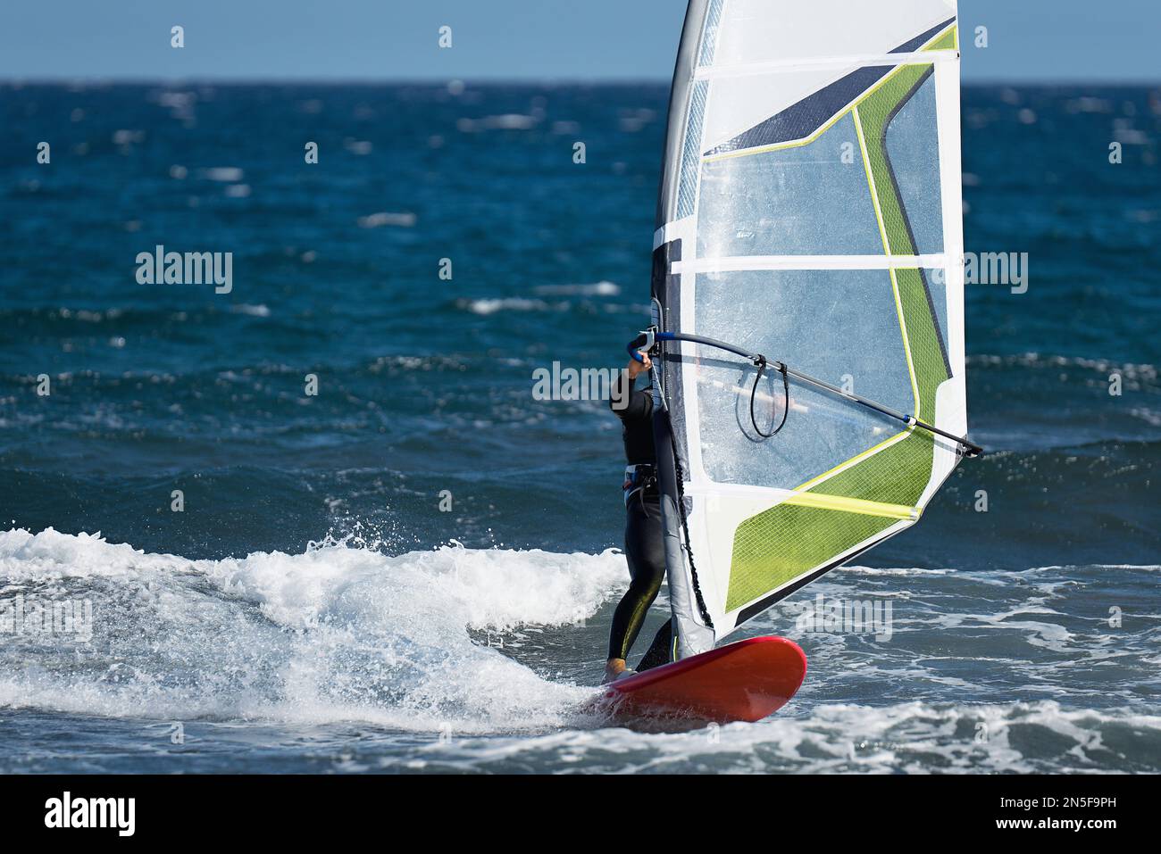 Windsurfer surfen im Wind auf Wellen im Meer. Sportliche Freizeitaktivitäten Stockfoto