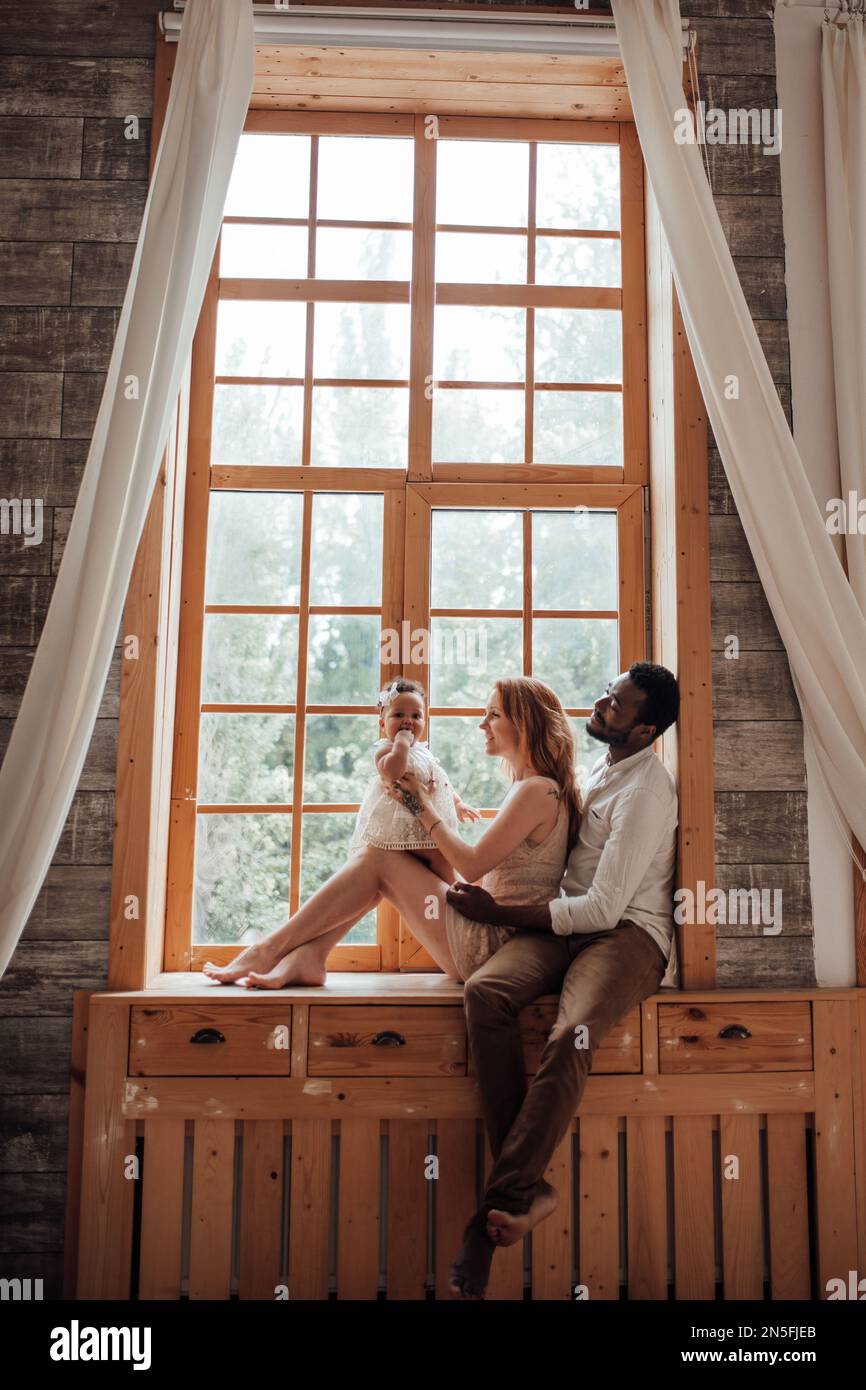 Gemischte Familien mit dunkelhäutigen Kleinkindern verbringen Zeit miteinander. Nutzen Sie das helle Fenster in der gemütlichen Wohnung. Ein afroamerikaner, seine schöne Frau und Stockfoto Gemischte Familien mit dunkelhäutigen Kleinkindern verbringen Zeit miteinander. Nutzen Sie das helle Fenster in der gemütlichen Wohnung. Ein afroamerikaner, seine schöne Frau und Stockfoto