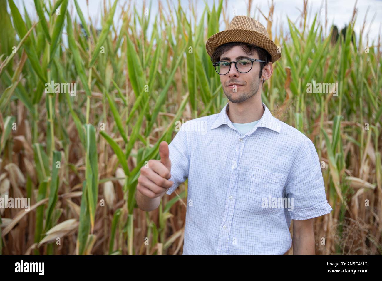 Ein zufriedener junger Bauer mit erhobenen Daumen auf seinem Maisfeld Stockfoto