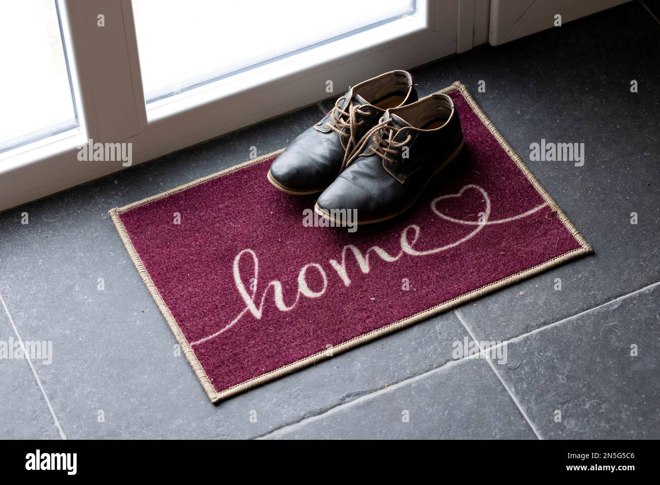 Ein Innenporträt mit zwei stilvollen blauen Schuhen, die auf einer Fußmatte neben der Eingangstür eines Hauses stehen. Perfekte Begrüßung für einen gue Stockfoto