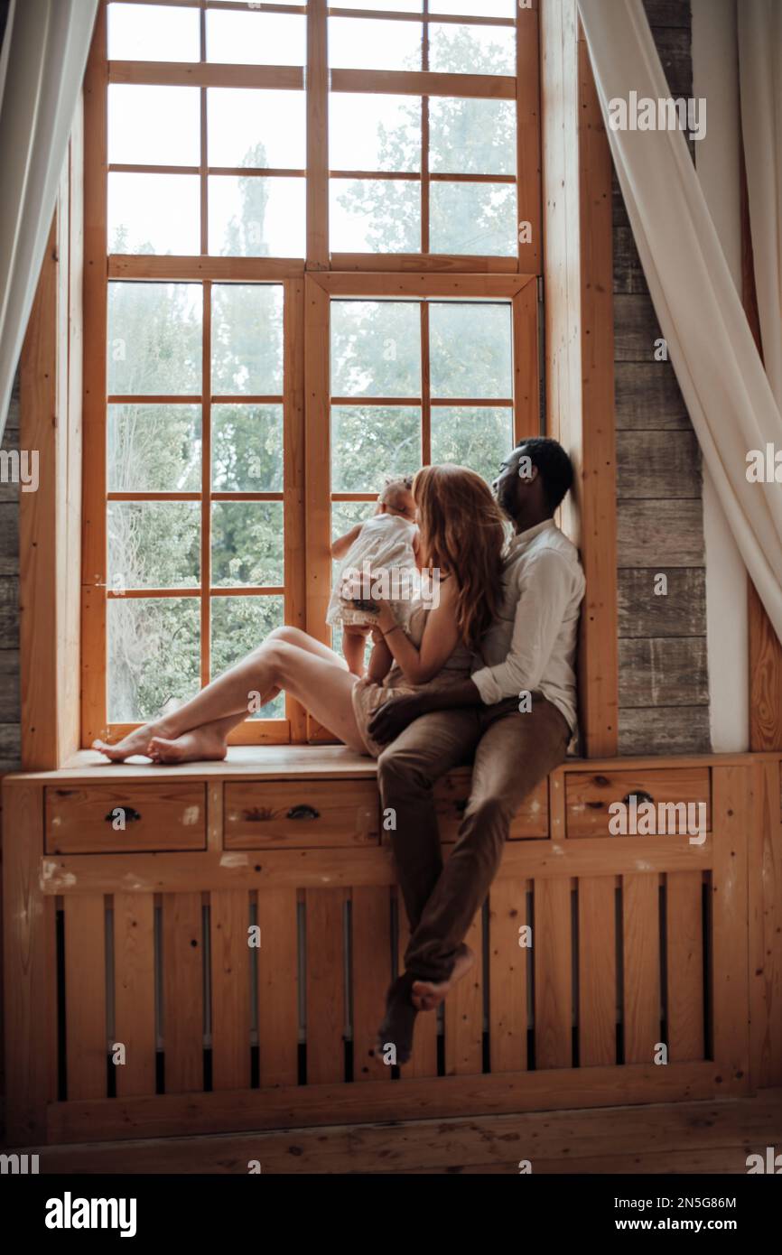 Gemischte Familien mit dunkelhäutigen Kleinkindern verbringen Zeit miteinander. Nutzen Sie das helle Fenster in der gemütlichen Wohnung. Ein afroamerikaner, seine schöne Frau und Stockfoto Gemischte Familien mit dunkelhäutigen Kleinkindern verbringen Zeit miteinander. Nutzen Sie das helle Fenster in der gemütlichen Wohnung. Ein afroamerikaner, seine schöne Frau und Stockfoto