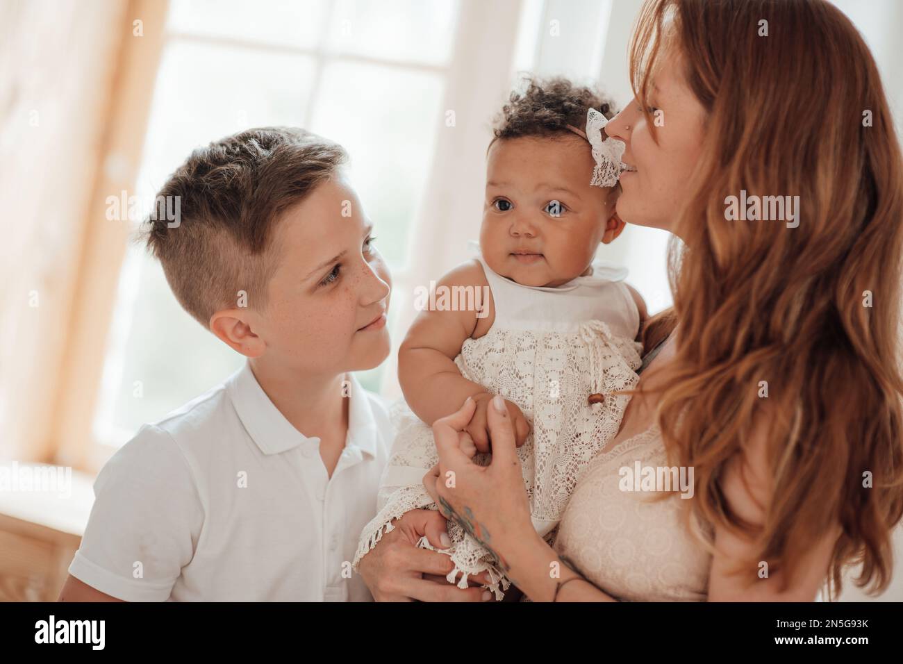 Gemischte Familie mit weißem Sohn und Tochter, die sich in einer gemütlichen Wohnung befindet. afroamerikanisches Baby mit seiner hellhäutigen mutter OL Stockfoto