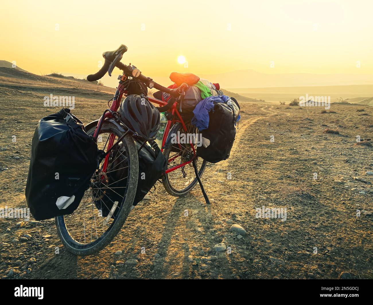 Das rote Fahrrad ist mit Taschen beladen und liegt am Straßenrand, umgeben von Bergen in der Landschaft des VAshlovani Nationalparks. Fahrradtouren in Geo Stockfoto